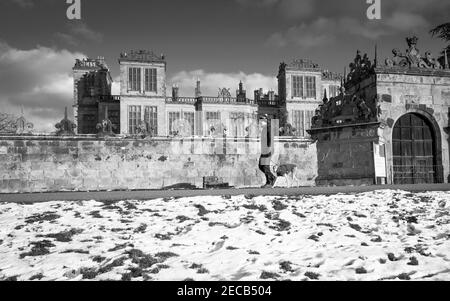Mann mit seinem Whippet auf einer kleinen Landstraße mit Schnee vor Hardwick Hall, Derbyshire. Stockfoto