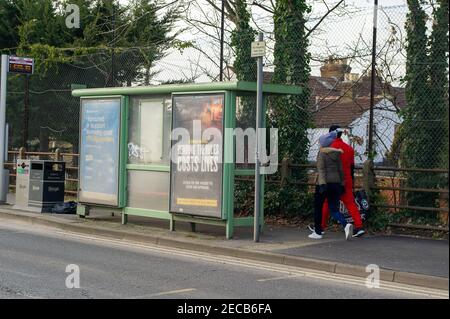 Slough, Berkshire, Großbritannien. 13th. Februar 2021. Ein Paar geht an einer Regierung Covid-19 vorbei und beugt sich den Regeln, kostet Leben Werbung an einer Bushaltestelle. Obwohl die rollierende Seven-Day-Rate der positiven Covid-19-Fälle um 44% in der Seven-Day-Rolling-Rate bis zum 6th. Februar 2021 gesunken ist, hat Slough weiterhin eine der höchsten Raten an positiven Covid-19-Raten in Berkshire. Quelle: Maureen McLean/Alamy Live News Stockfoto