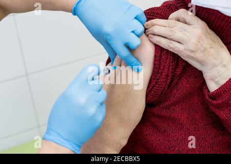 Arzt in Schutzhandschuhen hält Spritze und macht Injektion zu älteren Patienten.Ältere Impfkonzept. Medizinisches Personal, das einen älteren Menschen impft Stockfoto