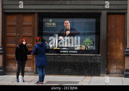 Dublin, Irland. Februar 2021, 12th. Zwei Frauen unterhalten sich vor einem geschlossenen Dunnes Store mit einem Bild des berühmten Küchenchefs Neven McGuire im Zentrum von Dublin während der Pandemiesperre COVID-19.die Sperrbeschränkungen der Stufe 5 sollen von der irischen Regierung verlängert werden. Um mindestens sechs weitere Wochen, in denen nur Schulen und der Bausektor voraussichtlich noch vor Ostern wieder eröffnet werden dürfen. Quelle: Cezary Kowalski/SOPA Images/ZUMA Wire/Alamy Live News Stockfoto