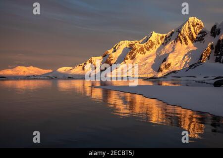 Der goldene Sonnenuntergang schmückt den eisigen Lemaire Channel in der abgelegenen Antarktis, wo Ruhe auf beeindruckende Schönheit trifft Stockfoto