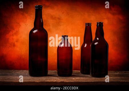 Vier dunkelbraune Glasbierflaschen auf einem Scheunenholz Tisch vor einem orangefarbenen Hintergrund Stockfoto