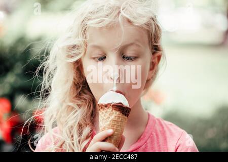 Nette lustige liebenswert Mädchen mit schmutzigen Nase essen Eis lecken. Kind, das Essen mit gekreuzten Augen anschaut. Urkomisch Kind essen lecker süßen kalten summ Stockfoto