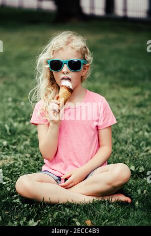 Nette lustige liebenswert Mädchen in Sonnenbrille mit schmutziger Nase und Schnurrbärte essen Eis aus Waffelkegel. Happy cool Hipster Kind essen lecker süß c Stockfoto