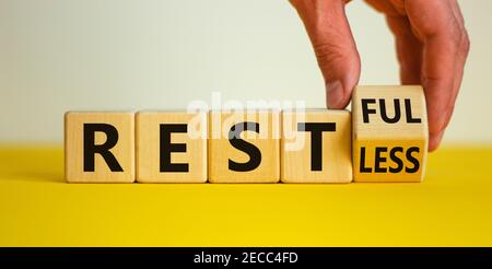 Symbol „Restless“ oder „RESTful“. Geschäftsmann dreht den Holzwürfel, ändert das Wort "stlos" in "stful". Schöner gelber Tisch, weißer Hintergrund, Polizist Stockfoto