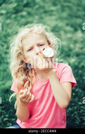 Cute lustige liebenswert Mädchen mit langen blonde chaotisch Haar essen Eis lecken aus Waffel-Kegel. Kinder essen leckere süße kalte Sommer Essen im Freien. Summe Stockfoto