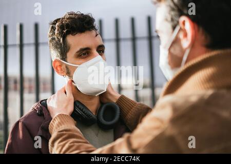 Nahaufnahme von zwei Homosexuell Jungs mit Gesichtsmasken auf Blick liebevoll auf einander, während einer berührt das Gesicht des anderen. Stockfoto