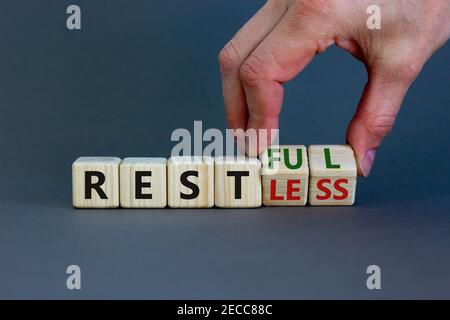 Symbol „Restless“ oder „RESTful“. Geschäftsmann dreht Holzwürfel, ändert das Wort "stlos" in "stful". Schöner grauer Tisch, grauer Hintergrund, Kopierer Stockfoto