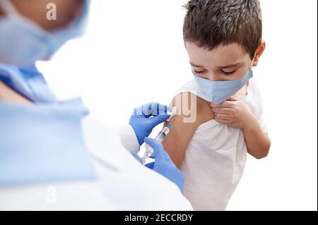 Erschrocken Junge schaut auf seine Hand, während Arzt ihn impfen. Isoliert auf weißem Hintergrund Stockfoto