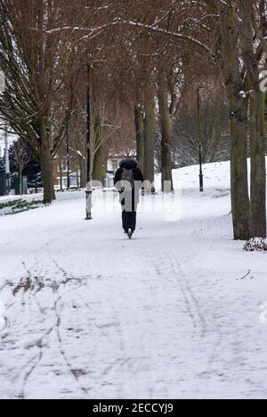 E Scooter Fahrer in Southend on Sea, Essex, UK, mit Schnee von Storm Darcy. Elektroroller wird durch bewaldeten Bereich auf Schnee in Victoria Ave geritten Stockfoto