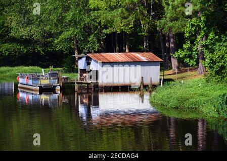 Raue Party Barge ist bis zu einem kleinen Dock gebunden. Zinngebäude dient als Bootshaus und Lagerung. Alle sitzen am White Oak Lake in South Arkansas. Stockfoto