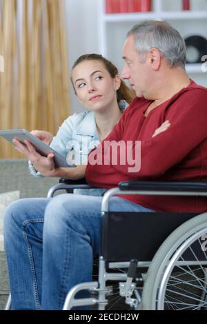 Junge Dame zeigt Tablet-Bildschirm zu behinderten Mann Stockfoto