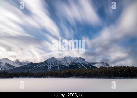 Wirbelnde Wolken am späten Morgen über dem schneebedeckten, gefrorenen Herbert Lake im Banff National Park im Januar. Stockfoto