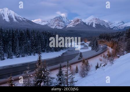 Blue Hour bei Morant's Curve während eine Langzeitaufnahme zeigt, wie der Canadian Pacific Zug rollt, indem er die verschneiten Wälder an der Eisenbahnseite beleuchtet. Stockfoto