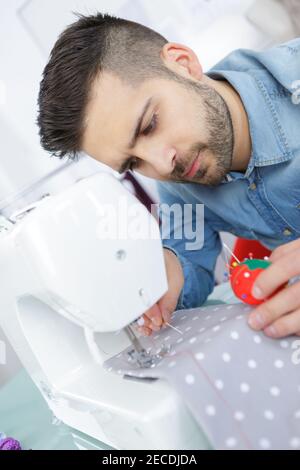 Junger Mann mit Nähmaschine und halten Stift Kissen Stockfoto