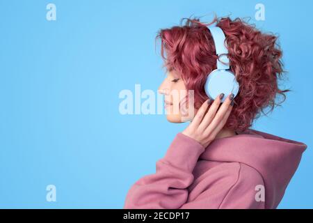 Profilansicht Porträt von verträumten jungen rosa Haar Mädchen tragen in lässiger Kleidung, genießen Sie Sound und Musik hören in Kopfhörern stehen gegen blau Stockfoto