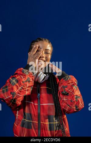 Vertikales Porträt einer jungen afroamerikanischen Frau, die fröhlich lächelt Blauer Hintergrund Stockfoto