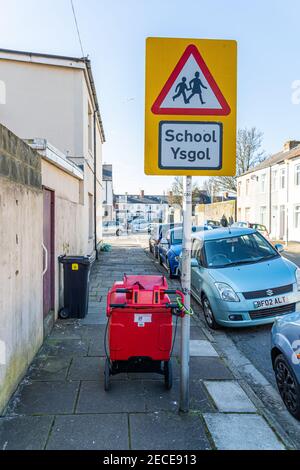 Cardiff, Wales - Februar 12th 2021: Der Trolley eines Postpersonals ist an einem Schulstraßenschild auf einem Bürgersteig in einer Straße verriegelt Stockfoto