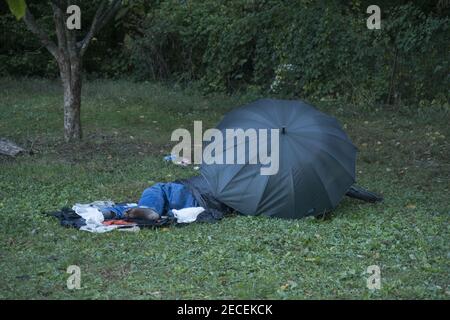 Verhmmelte Obdachlose, die unter einem Regenschirm im Prospect Park, Brooklyn, New York, schlafen. Stockfoto