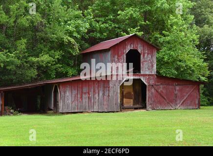 Rote, verwitterte Holzscheune steht auf einem kleinen Bauernhof in Arkansas. Loft ist offen. Es steht am Waldrand. Stockfoto