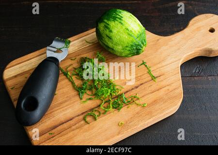 Zesting a Lime on a Wood Cutting Board: Eine zested lime mit Limettenschale und ein Zester auf einem hölzernen Schneidebrett Stockfoto