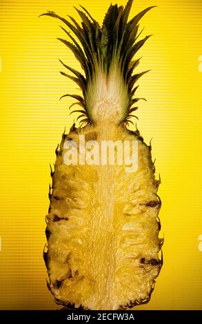 Eine frische Ananas, halbiert, steht gegen ein Gelb Hintergrund Stockfoto
