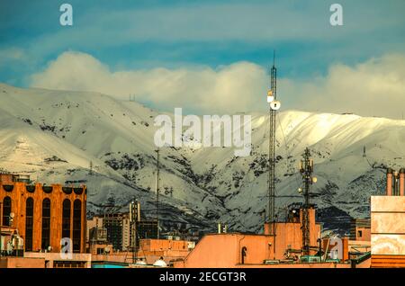 Schneebedeckte Tochal Berge vor einem blauen Himmel mit dicken Wolken Am Fuße der dicht bebauten Stadt Teheran Stockfoto