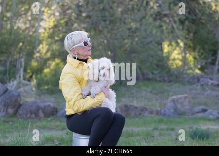 Eine ältere Frau und ihr Pudel genießen die Natur an einem kühlen Frühlingstag. Stockfoto