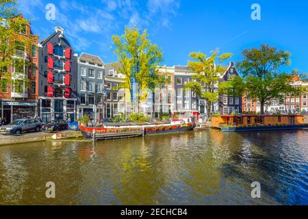 Bunte Hausboote säumen den Kanal vor bunten niederländischen Häusern an einem sonnigen Tag im frühen Herbst in Amsterdam, Niederlande Stockfoto