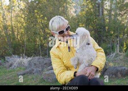 Eine ältere Frau und ihr Pudel genießen die Natur an einem kühlen Frühlingstag. Stockfoto