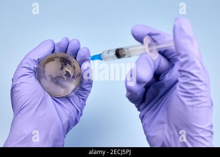 Die Hände der Frau in medizinischen Handschuhen halten einen Planeten Erde Globus und eine Spritze, das Konzept der Impfung. Stockfoto