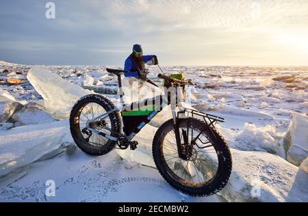 Der Mann hat eine Teebremse in der Nähe des Fahrrads bei Frozen see bei Sonnenuntergang in Kasachstan Stockfoto