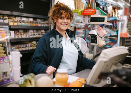 Frau an der Kasse im Supermarkt. Der Angestellte an der Kasse lächelte der Kamera zu. Stockfoto