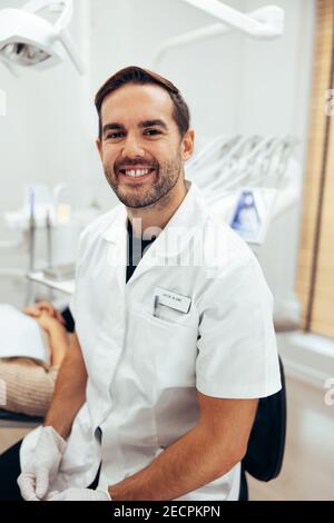 Porträt eines selbstbewussten Zahnarztexperten in seiner Klinik. Zahnarzt mit Laborkittel, der die Kamera anschaut und lächelt. Stockfoto