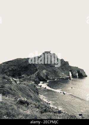 Eine vertikale Graustufenaufnahme eines verlassenen Gebäudes auf der Oberseite Der Klippe in der Nähe des Meeres Stockfoto