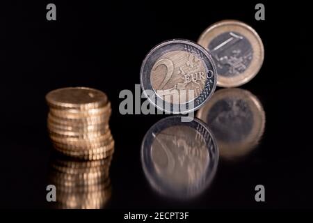 Euro-Münzen isoliert mit pechschwarzem Hintergrund, reflektierend in schwarzer Metallic-Oberfläche. Geld auf einem sehr dunklen Tisch. Stockfoto