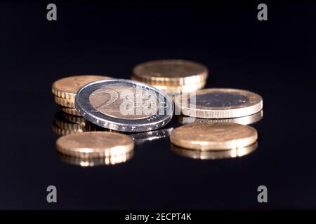 Euro-Münzen isoliert mit pechschwarzem Hintergrund, reflektierend in schwarzer Metallic-Oberfläche. Geld auf einem sehr dunklen Tisch. Stockfoto