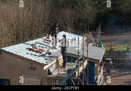 Zwei Arbeiter, die ein Schiefer-Fliesendach auf einer von Gerüsten umgebenen Baustelle in Rural Devon, England, Großbritannien, ersetzen Stockfoto