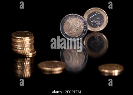 Euro-Münzen isoliert mit pechschwarzem Hintergrund, reflektierend in schwarzer Metallic-Oberfläche. Geld auf einem sehr dunklen Tisch. Stockfoto
