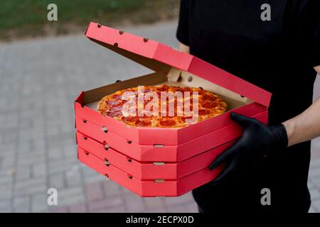 Lebensmittelkurier in schwarzen medizinischen Handschuhen hält 4 rote Boxen mit Pizza aus der Pizzeria. Lebensmittellieferung bei Quarantäne Coronavirus covd-19 Zeitraum. Stockfoto