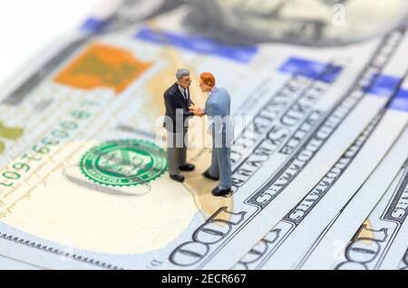Geschäftsleute schütteln Hände auf amerikanischen Dollar. Geschäftsleute Figuren auf Geld Hintergrund. Finanzwachstum. Geschäftsgewinn- oder Ertragskonzept. Kaufen und verbuchen Stockfoto