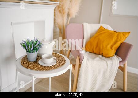 Stilvolle elegante Öko Zusammensetzung Wohnzimmer mit weißem Frühstückstisch Kaffeetasse Teekanne falschen Kamin getrocknete Blumen Pflanzen Pampas Gras rosa Pulver Sessel, Decke und Kissen. Moderne Inneneinrichtung. Stockfoto