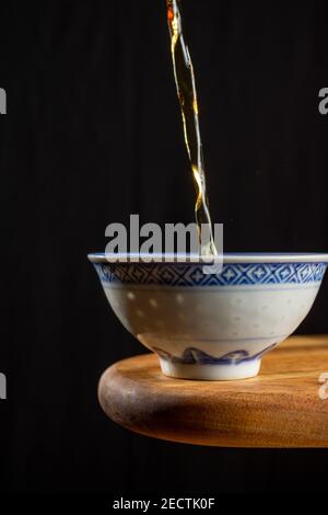 Nahaufnahme von Tee, der in china Tasse fällt, auf Holztisch, schwarzer Hintergrund, vertikal, mit Kopierraum Stockfoto