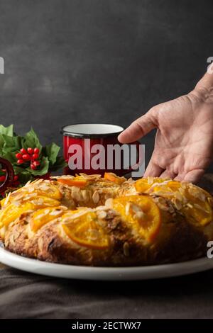 Draufsicht auf hausgemachten Roscon de Reyes, auf weißem Teller, mit Frauenhand, mit roter Tasse und schwarzem Hintergrund, vertikal Stockfoto