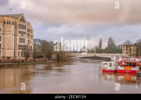 Lendal Brücke in York mit alten und modernen Gebäuden auf jeder Seite. Ausflugsboote liegen in der Nähe der Brücke und der Fluss ist in Überschwemmung. Stockfoto