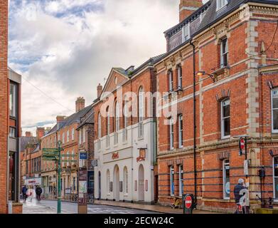 Straßenszene in der Stadt. Zwei Fußgänger gehen die Straße hinunter und ein Bettler sitzt auf dem Bürgersteig. Im Vordergrund spricht ein Mann am Telefon. Stockfoto