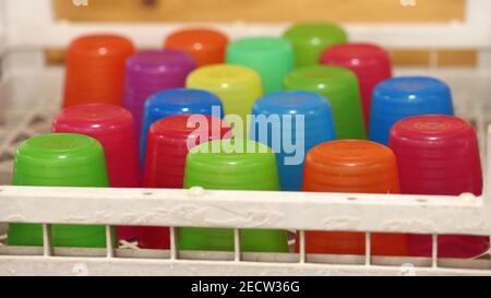 Viele bunte Trinkgläser aus rotem, orangefarbenem, gelbem, blauem und grünem Kunststoff. Einfache, lebendige und lustige Tassen, die Erinnerungen an die Kindheit zurückbringen Stockfoto