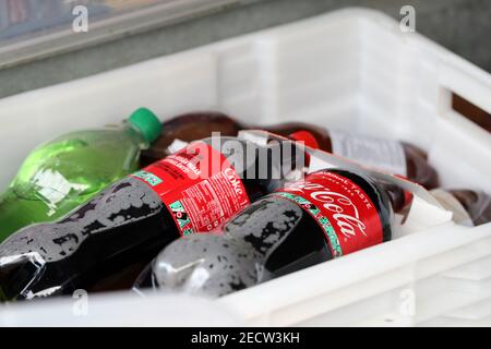 Mehrere große Coca-Cola-Flaschen aus Kunststoff und einige andere Limonadenflaschen in einem großen weißen Behälterkasten. Ungesunde, aber leckere Getränke. Nahaufnahme. Stockfoto