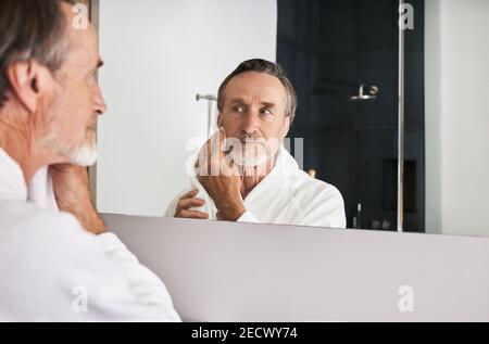 Älterer Mann, der sein Gesicht mit einem Handtuch vor sich abwischt Von einem Spiegel im Badezimmer Stockfoto