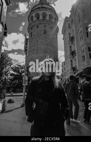 Eine vertikale Graustufenaufnahme einer Frau aus dem Nahen Osten, die vor dem Galata-Turm in Istanbul, Türkei, steht Stockfoto